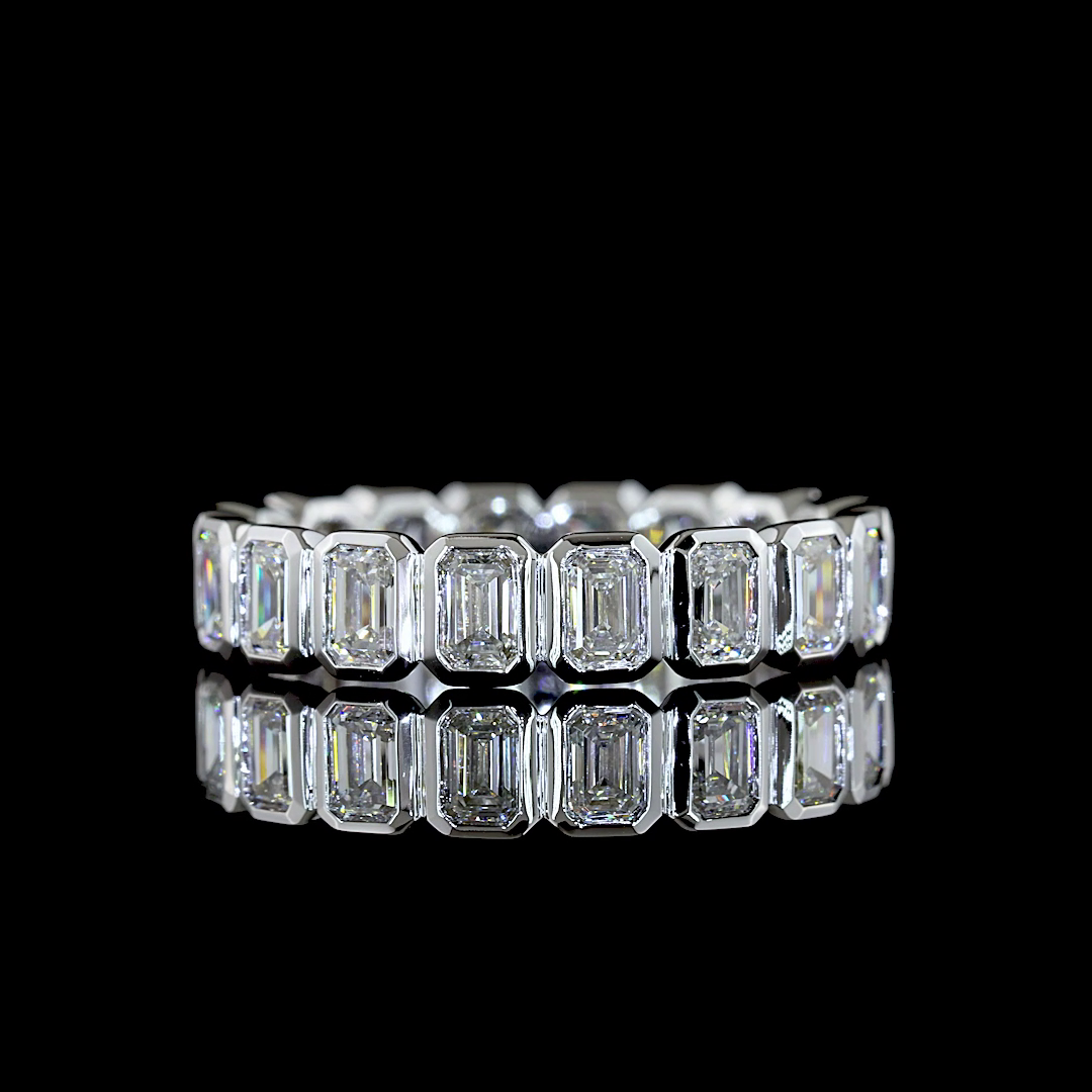 Lab grown emerald cut diamond eternity band in a white gold bezel setting on a black background.