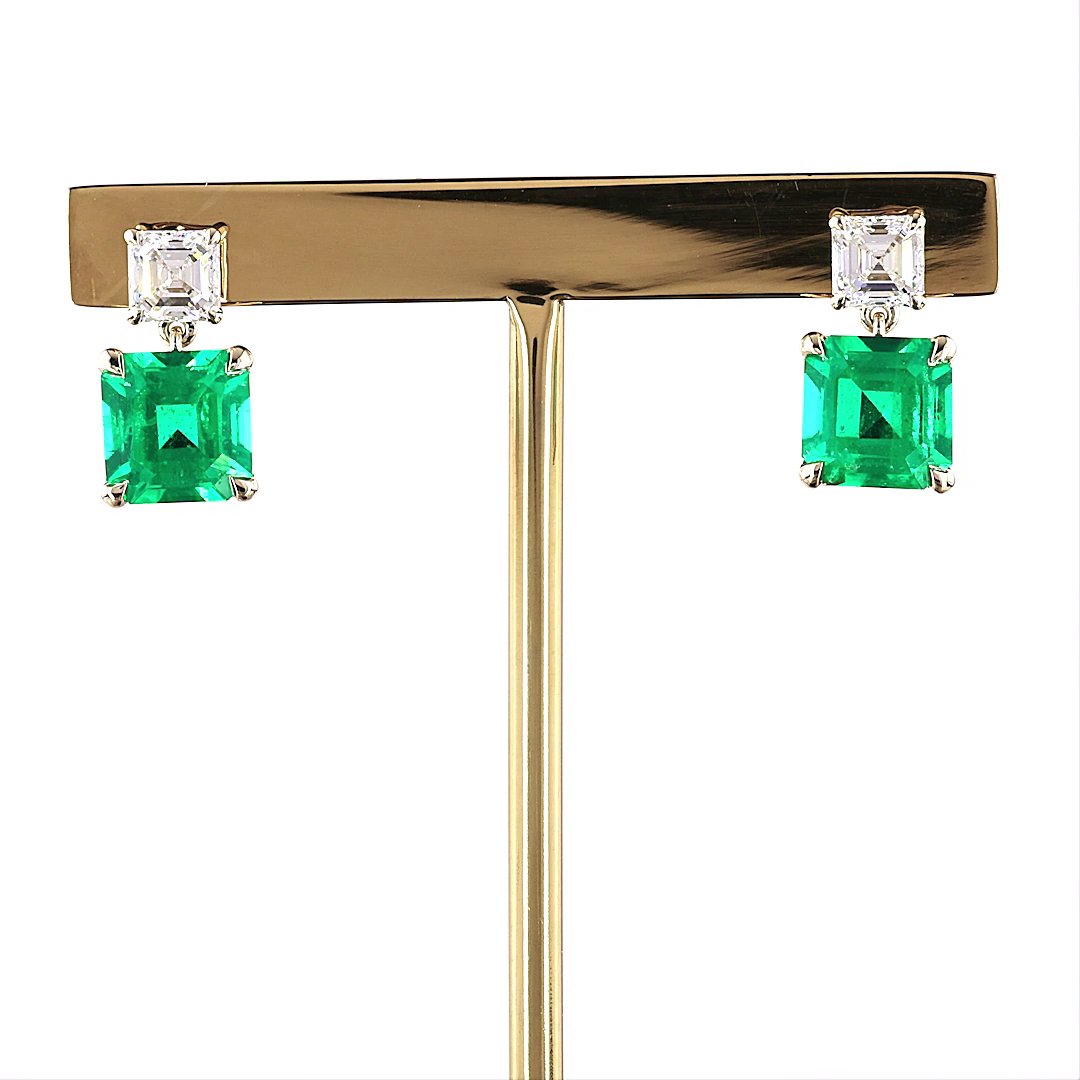 5.65ctw lab grown diamond and emerald drop earrings in 14k yellow gold on a display stand.
