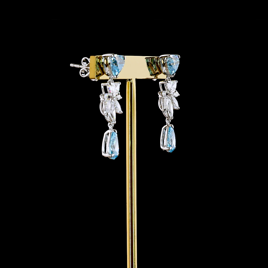 Lab grown diamond chandelier earrings with blue and white stones in 14k white gold on a gold stand.