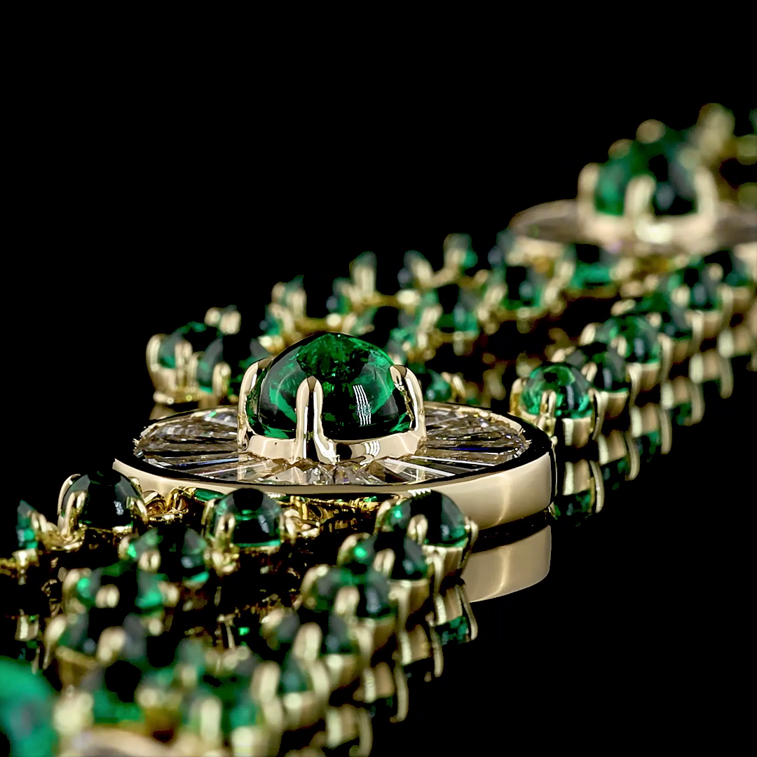 Close-up of a 14k yellow gold necklace with cabochon lab grown emeralds and diamond medallions.
