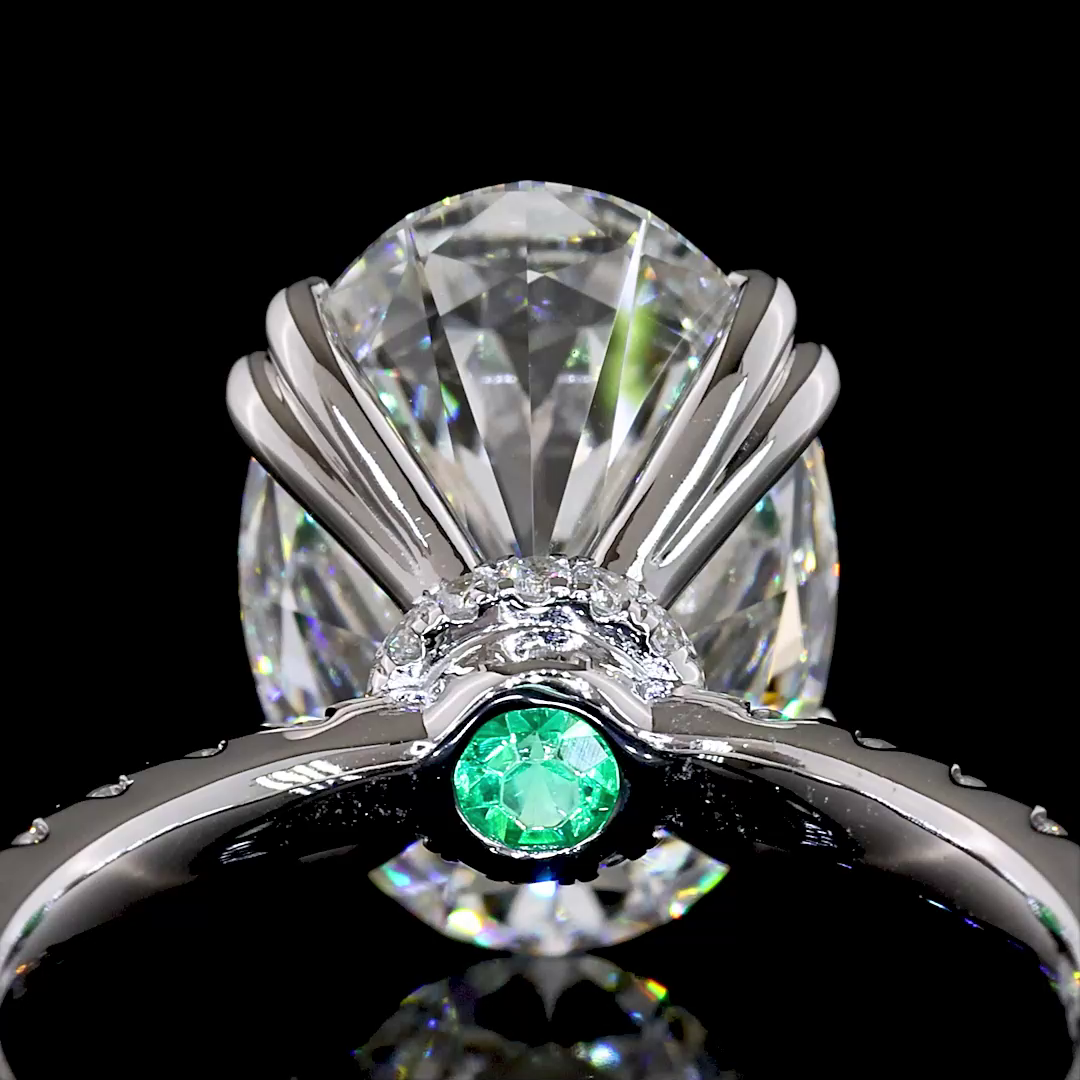 Close-up of a white gold ring featuring a large oval diamond and a hidden green emerald accent.