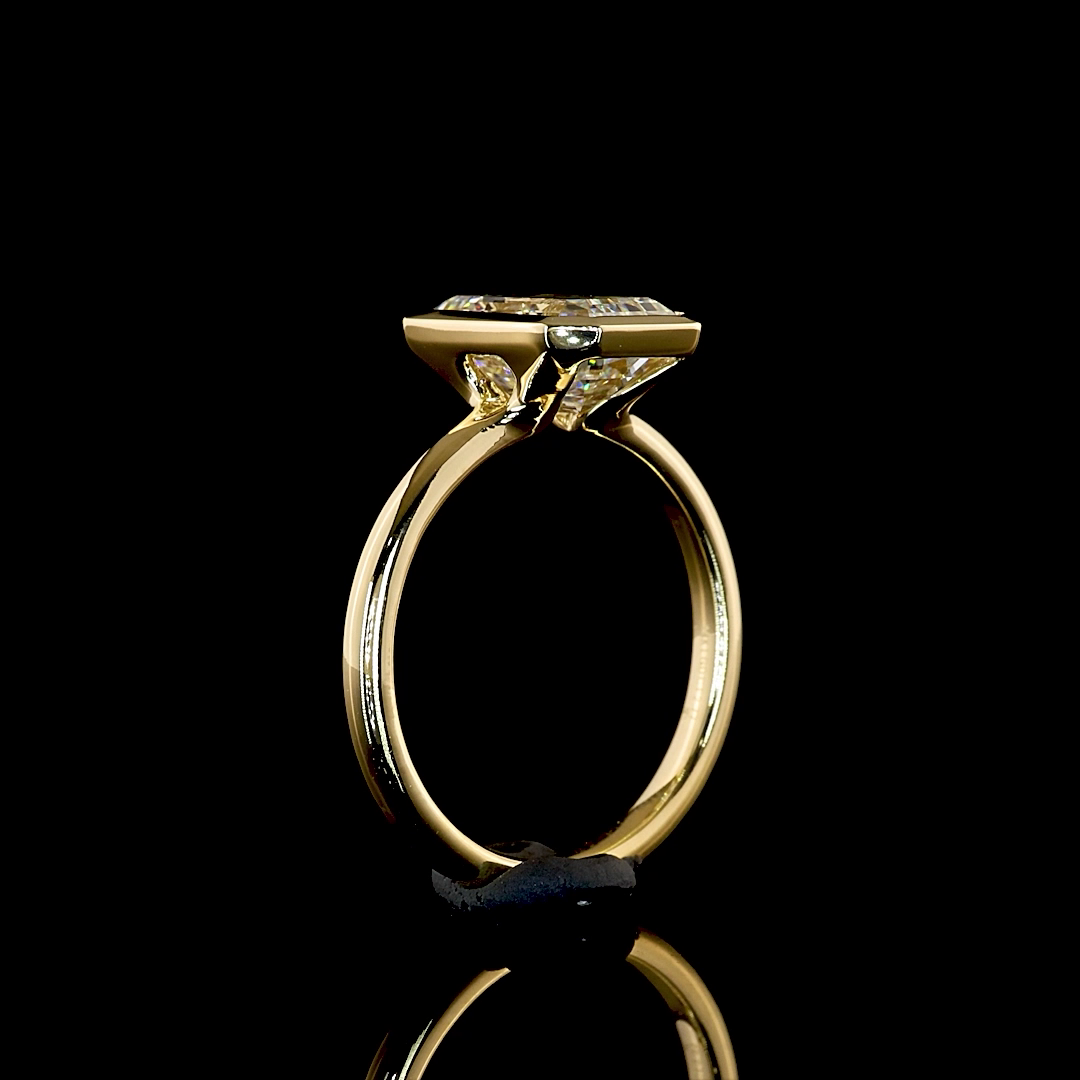 Side view of a 2.77ct emerald cut lab grown diamond engagement ring in a 14k yellow gold bezel set.