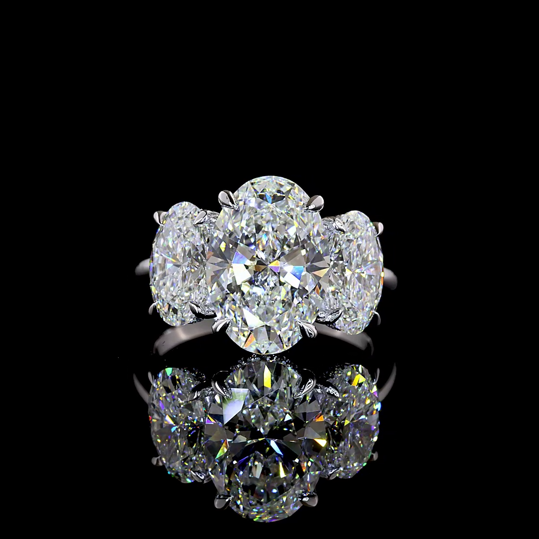 6.15ctw lab grown oval three stone engagement ring in 14k white gold on a black reflective surface.