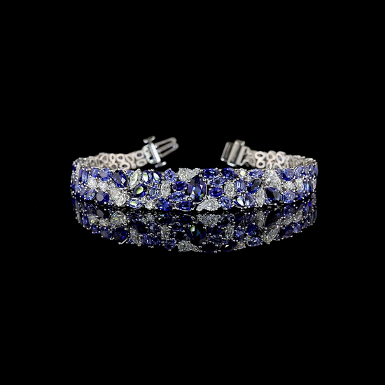 A white gold bracelet rotating on a black background. It is set with an array of lab grown sapphires and lab grown diamonds in various shapes and sizes, tapering down towards the bottom of the wrist. It has a secure tongue closure with a locking bar.