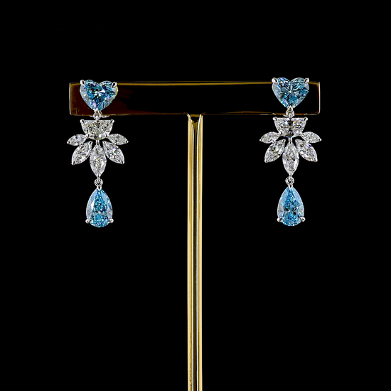 Lab grown diamond chandelier earrings made in 14k white gold, rotating on a brass stand in a 360 video with a black background. The earrings are set with a blue heart cut lab diamond at the post, followed by a cluster of halfmoon and marquise cut diamonds, with a pear cut lab grown blue diamond under that.