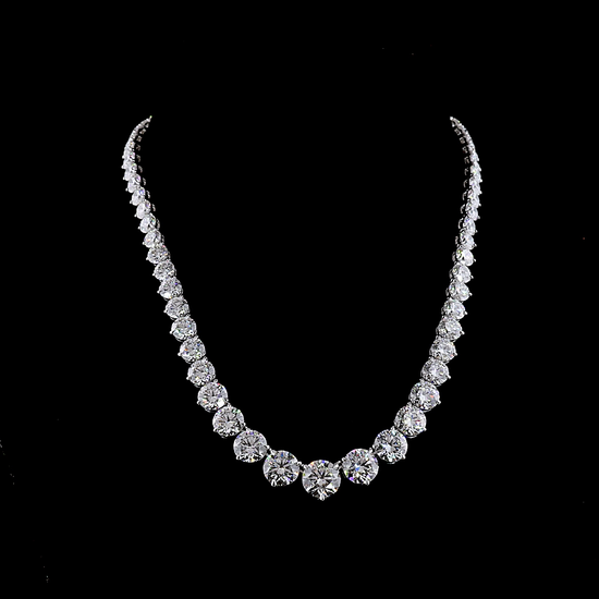 A 68.51ctw lab grown riviera necklace made in 14k white gold. Set with round lab grown diamonds, graduated by size with the largest stone in the front. The necklace is resting on a black bust, rotating on a black background.