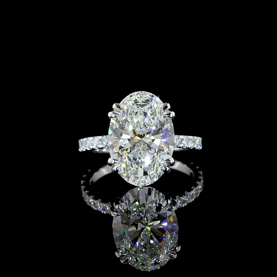 A 14k white gold engagement ring rotating in a 360 video on a black background. In the centre is set a 6.10ct oval cut lab grown diamond, with a small circle of lab diamonds under the stone and lab diamonds 3/4 distance around the band. Under the setting is set a lab grown emerald that rest against the finger when worn.