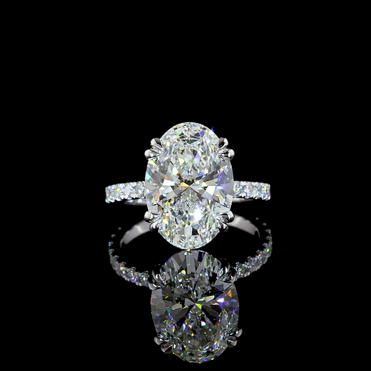 A 14k white gold engagement ring rotating in a 360 video on a black background. In the centre is set a 6.10ct oval cut lab grown diamond, with a small circle of lab diamonds under the stone and lab diamonds 3/4 distance around the band. Under the setting is set a lab grown emerald that rest against the finger when worn.