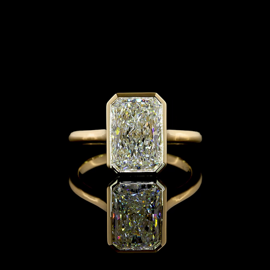 A 14k yellow gold engagement ring rotating in a 360 video on a black background. In the centre of the ring is a 3.17ct lab grown radiant cut diamond, bezel set. The gallery is a trellis style.