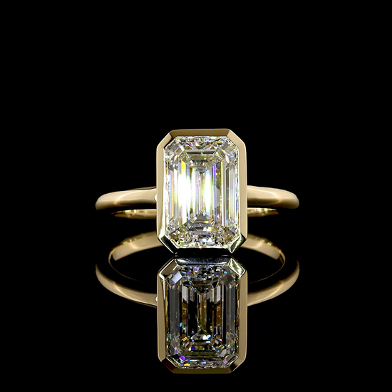 A 360 rotating video of a 14k yellow gold solitaire engagement ring, bezel set with a lab grown 2.77ct emerald cut diamond, on a black background.